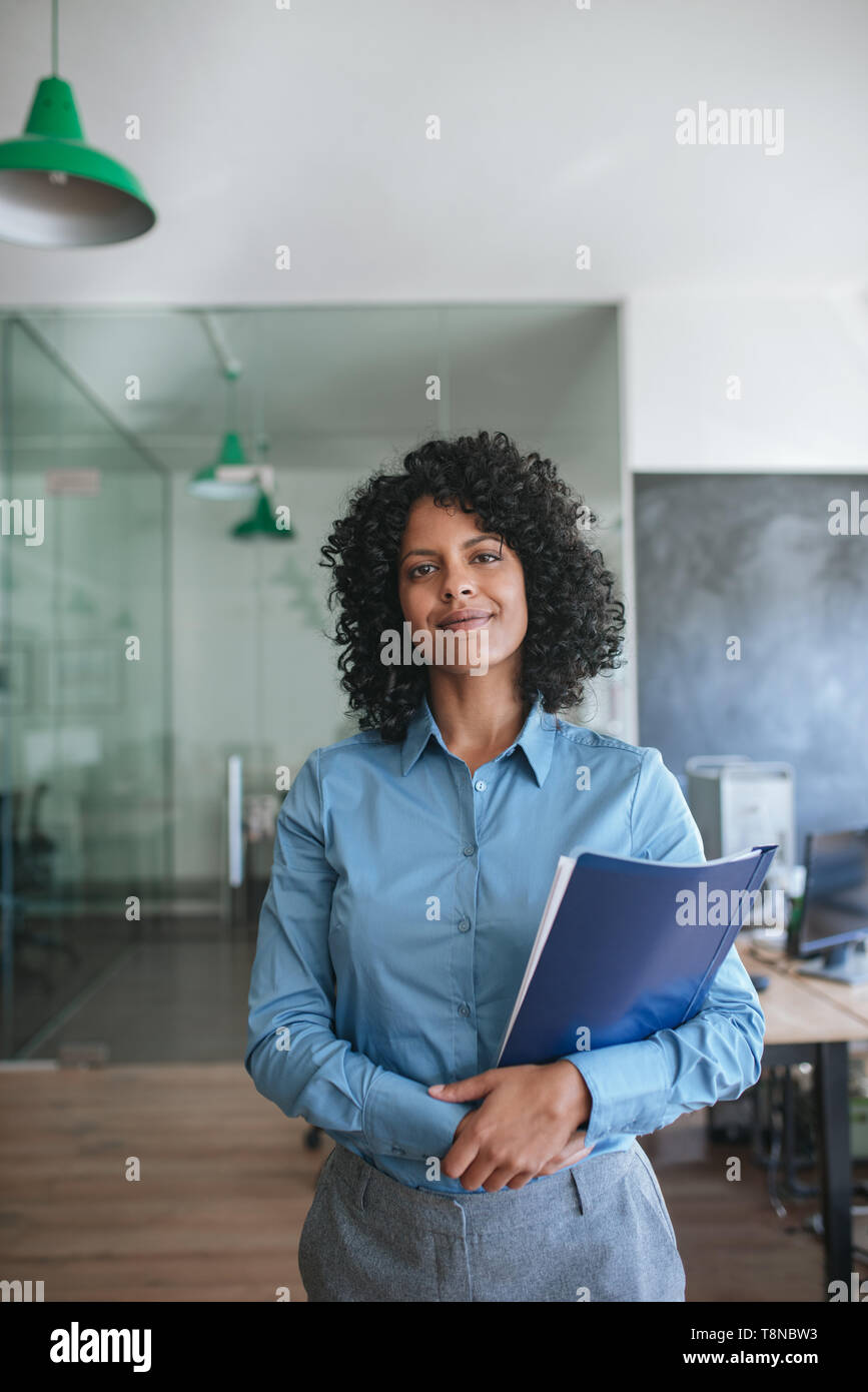 Sorridente giovane imprenditrice in piedi in un ufficio che trasportano i file Foto Stock