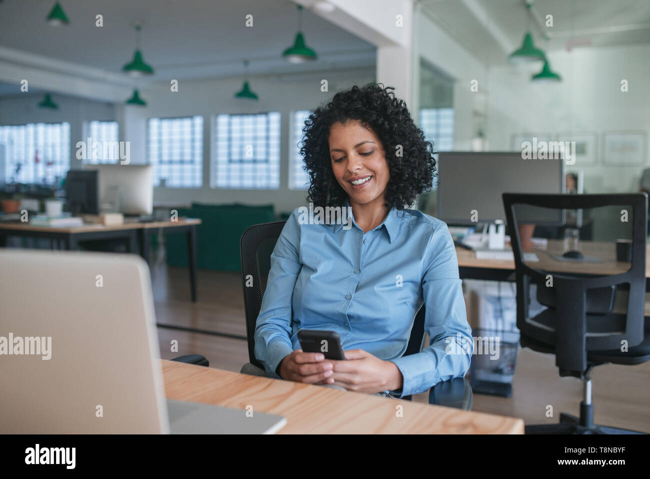 Imprenditrice sorridente seduto alla sua scrivania la lettura di un messaggio di testo Foto Stock