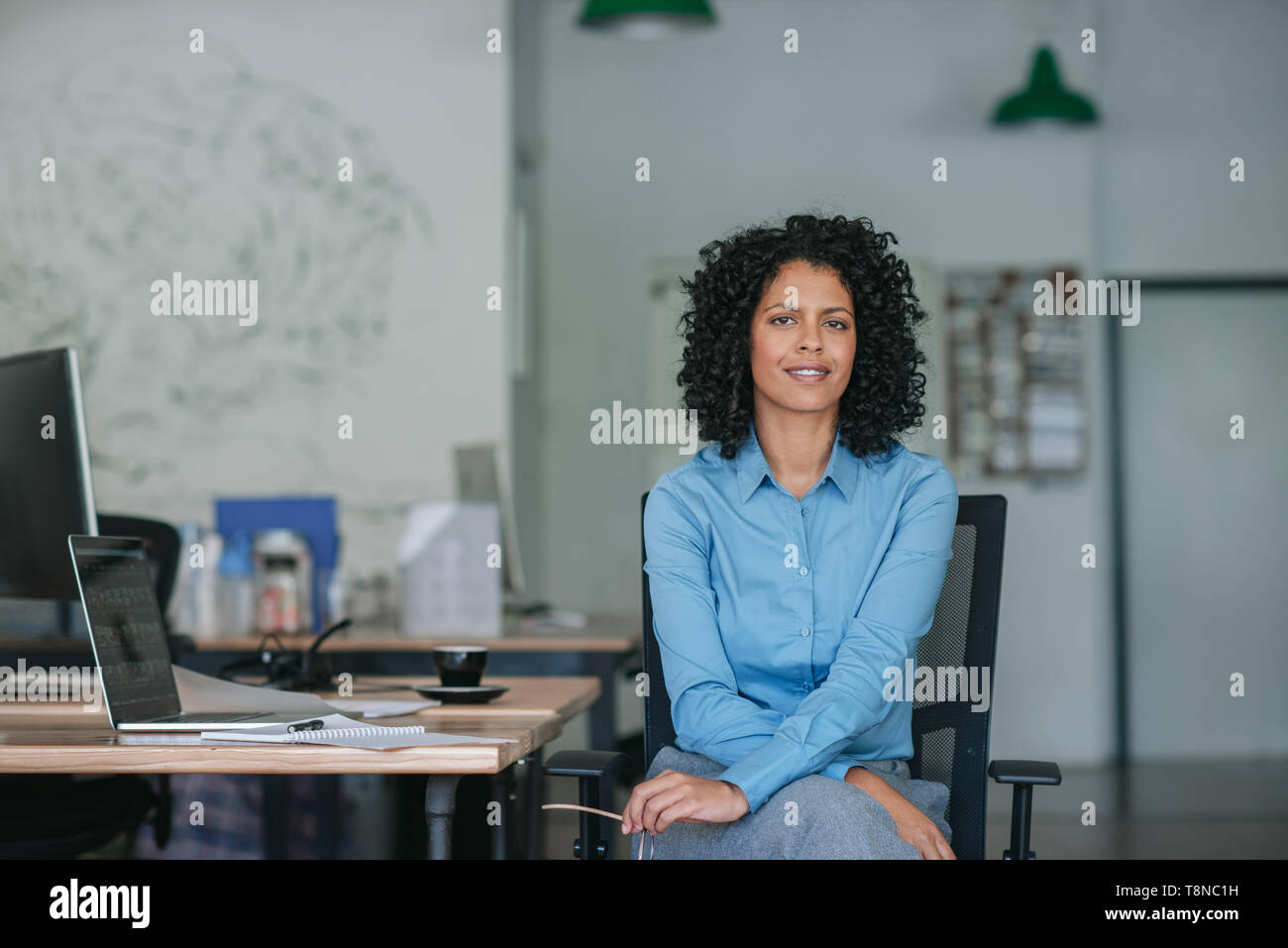 Sorridente giovane imprenditrice seduto alla sua scrivania in un ufficio Foto Stock
