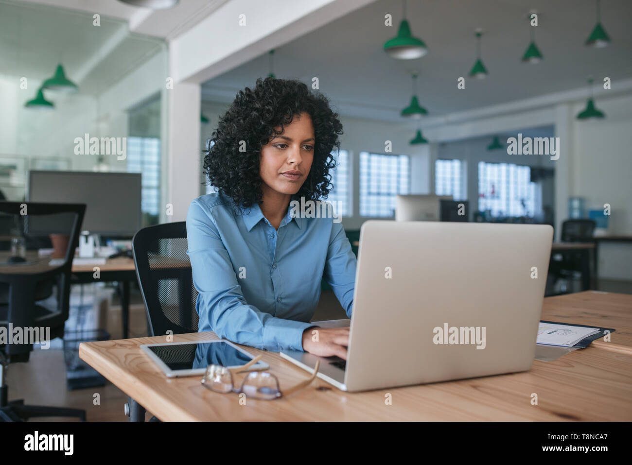 Focalizzato giovane imprenditrice usando un computer portatile presso il suo Ufficio escursioni Foto Stock