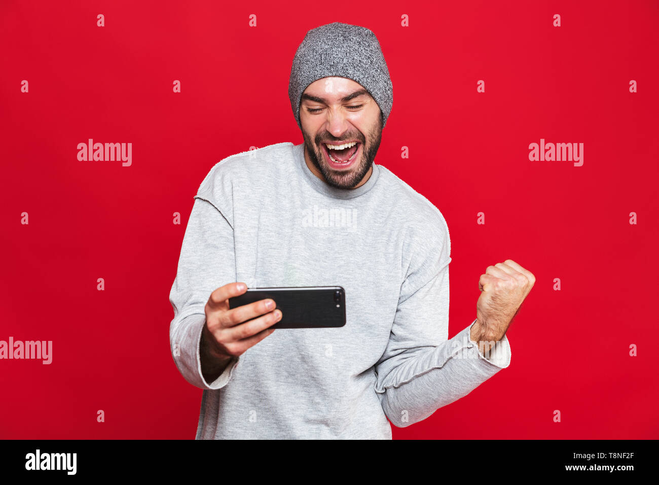 Immagine dell uomo unshaved 30s tenendo lo smartphone e la riproduzione di video giochi isolate su sfondo rosso Foto Stock
