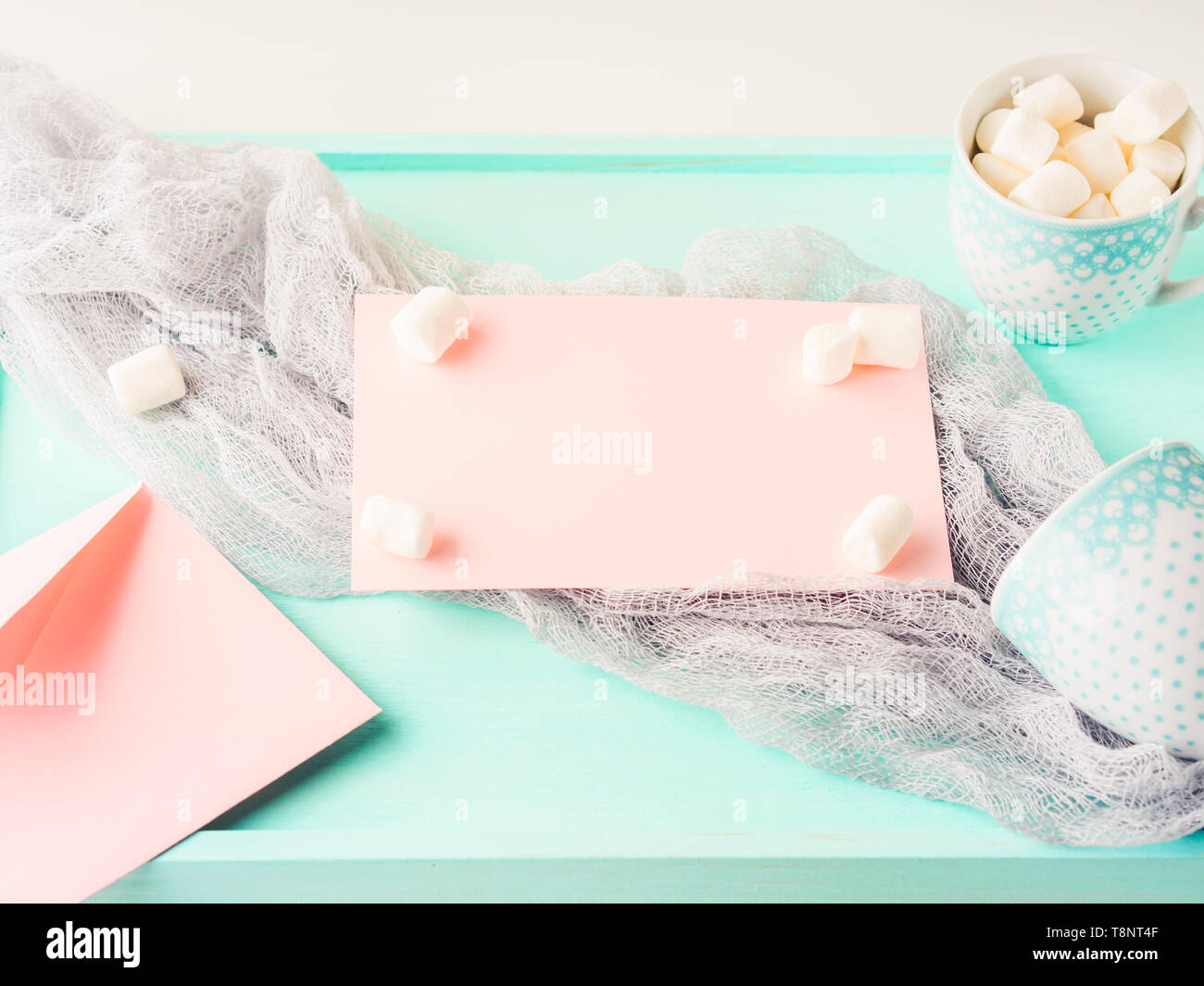 Carta rosa e marshmallows su sfondo turchese con busta e tazze da caffè. Colori pastello Foto Stock Carta rosa e marshmallows su sfondo turchese con busta e tazze da caffè. Colori pastello Foto Stock