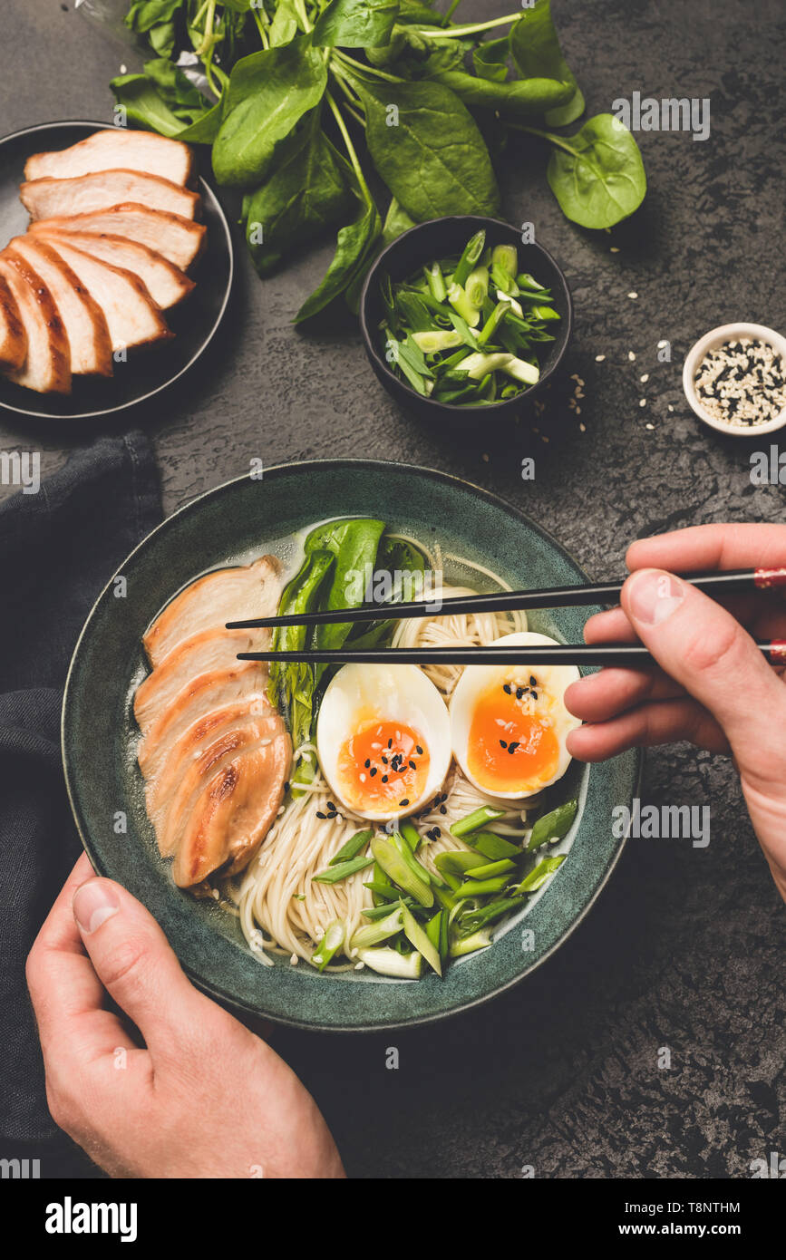 Mangiare giapponese ramen zuppa di noodle al pollo. Mano azienda bacchette al di sopra di una ciotola di zuppa asiatica. Nero lo sfondo di calcestruzzo Foto Stock