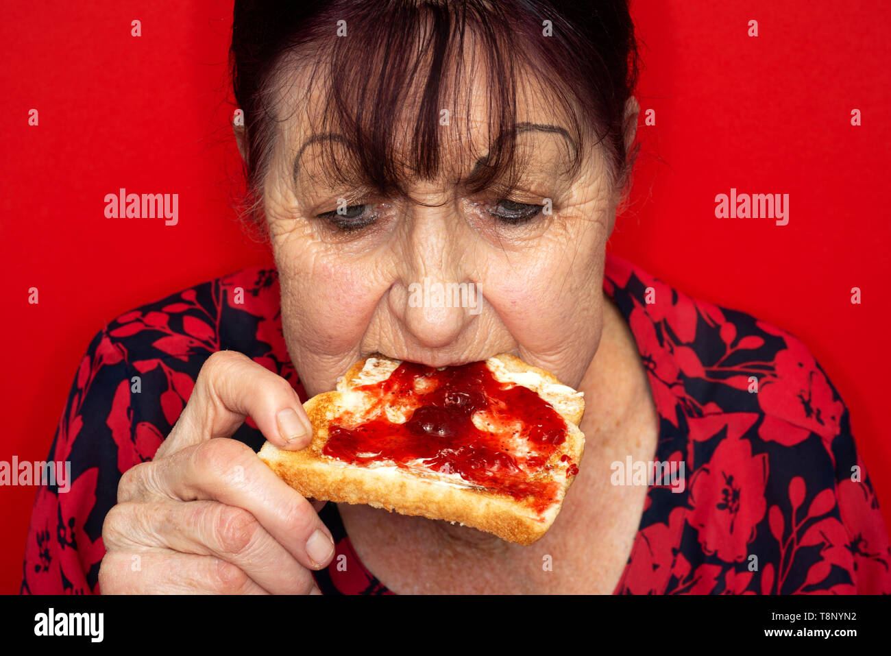 Donna anziana mangiare confettura di fragole su pane tostato Foto Stock