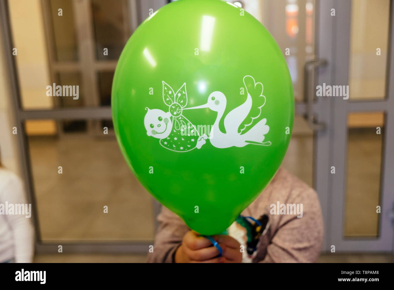 Ragazza con una palla verde nella sua mano con un disegno di una cicogna e un bambino in ospedale di maternità Foto Stock