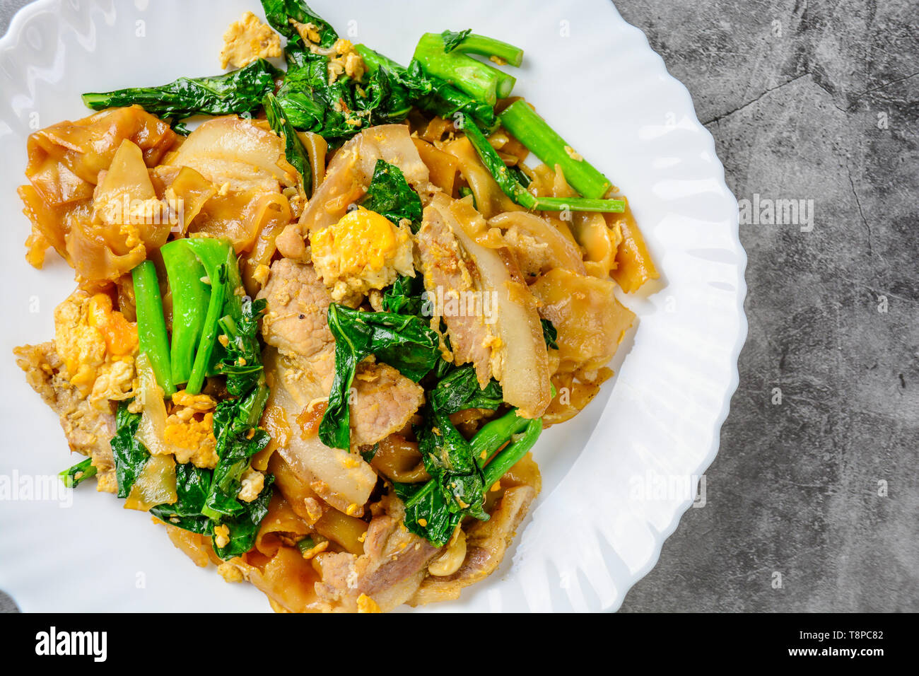 Saltati in padella il riso fresco-farina Tagliatelle con carne di maiale tagliata a fette, uovo e Kale. Quick noodle friggere. Foto Stock