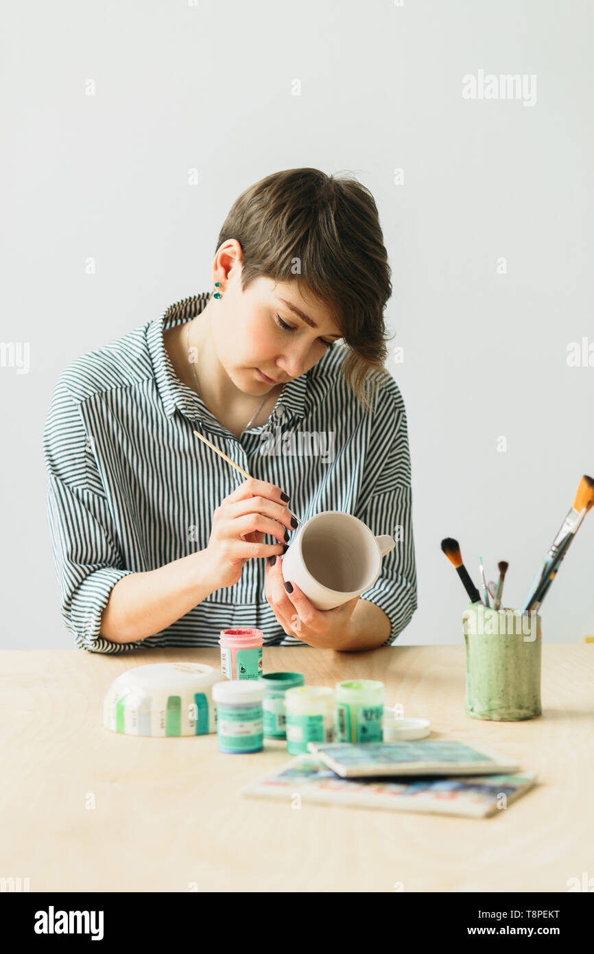 La ceramica donna tiene in mano una tazza di dipingere l'ornamento, di ceramica fatti a mano Foto Stock