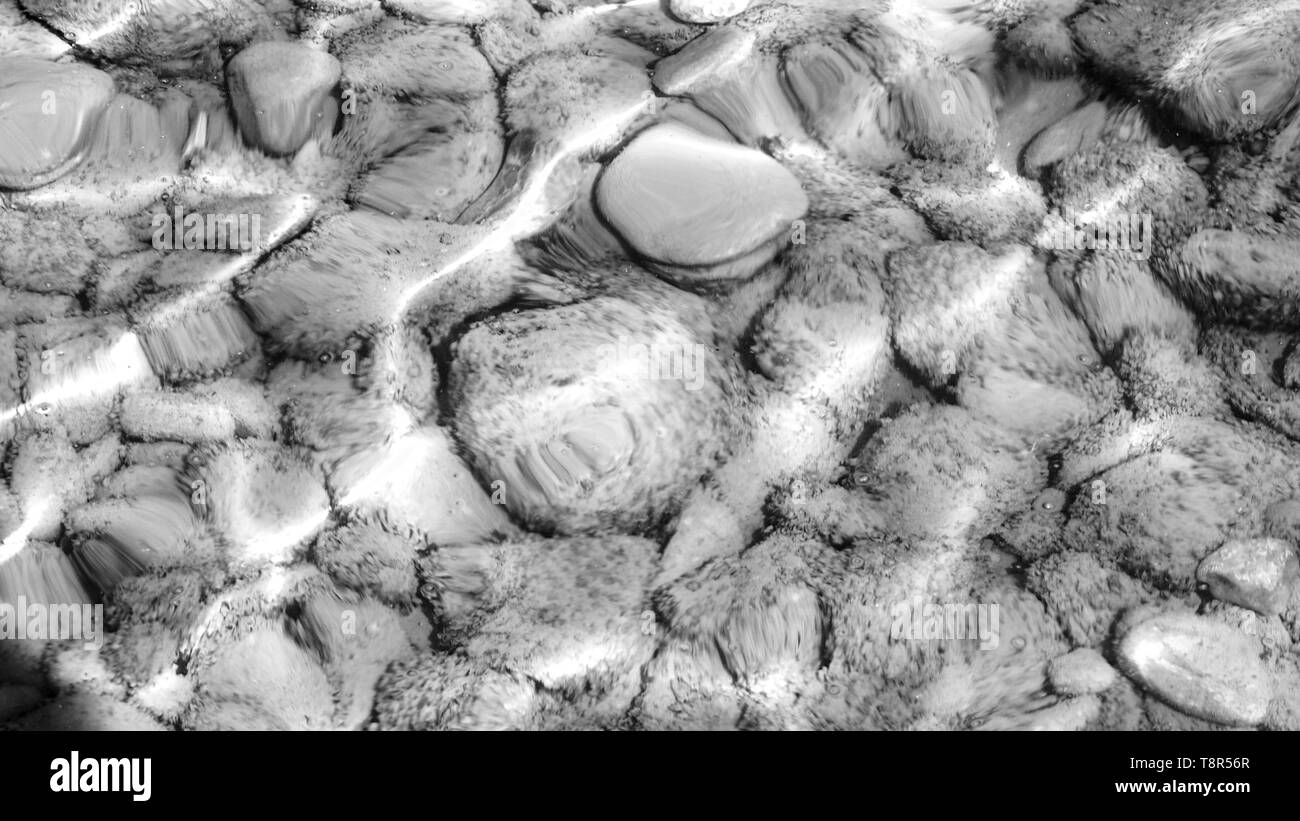 Vista del fondo di un lago,attraverso l acqua in sfumature di grigio.L'acqua è calma e si può vedere il round ghiaia lavata bene con la rifrazione Foto Stock