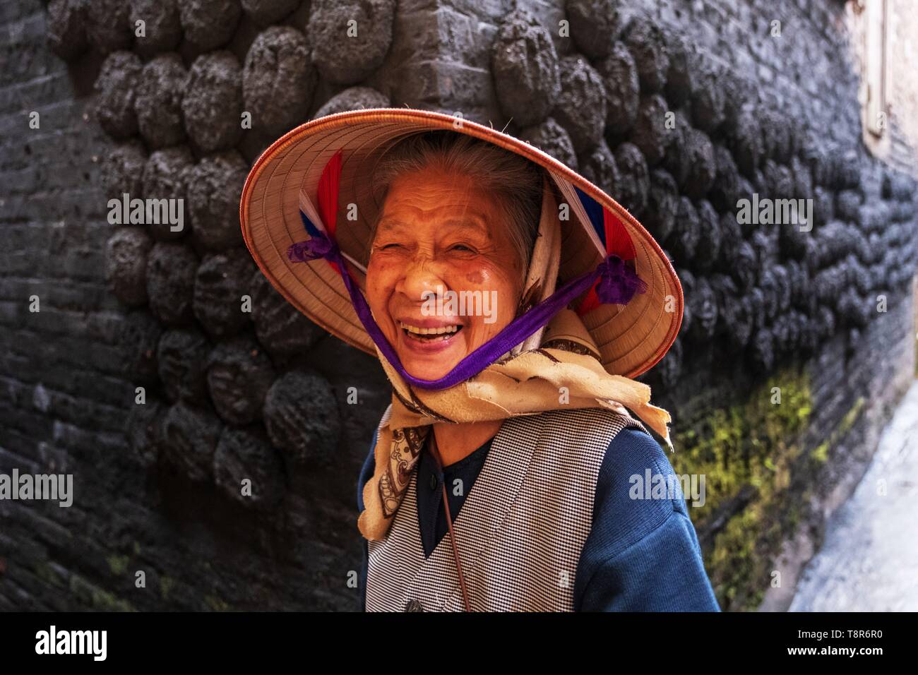 Il Vietnam, Bat Trang, vicino Hanoi, ceramista Village, Donna sorridente anteriore delle zolle di carbone bloccati su una parete di una casa tradizionale Foto Stock