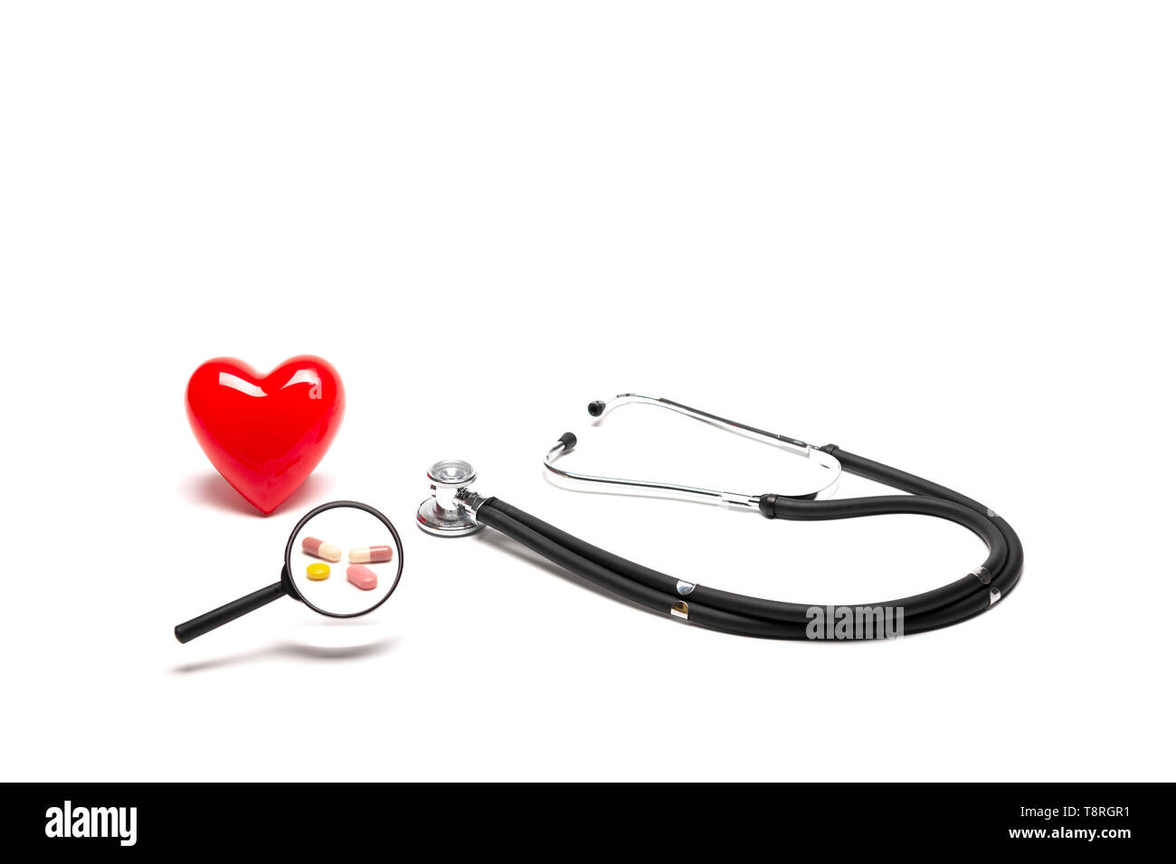 Vista frontale di plastica cuore rosso modello, stetoscopi, e farmaci con lente di ingrandimento su sfondo bianco, medico e un sano concetto. Foto Stock