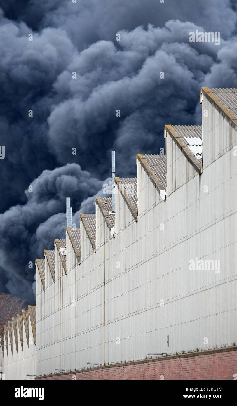 Nero pennacchi di fumo da un tossico incendi industriali come visto da dietro un edificio in fabbrica. Foto Stock