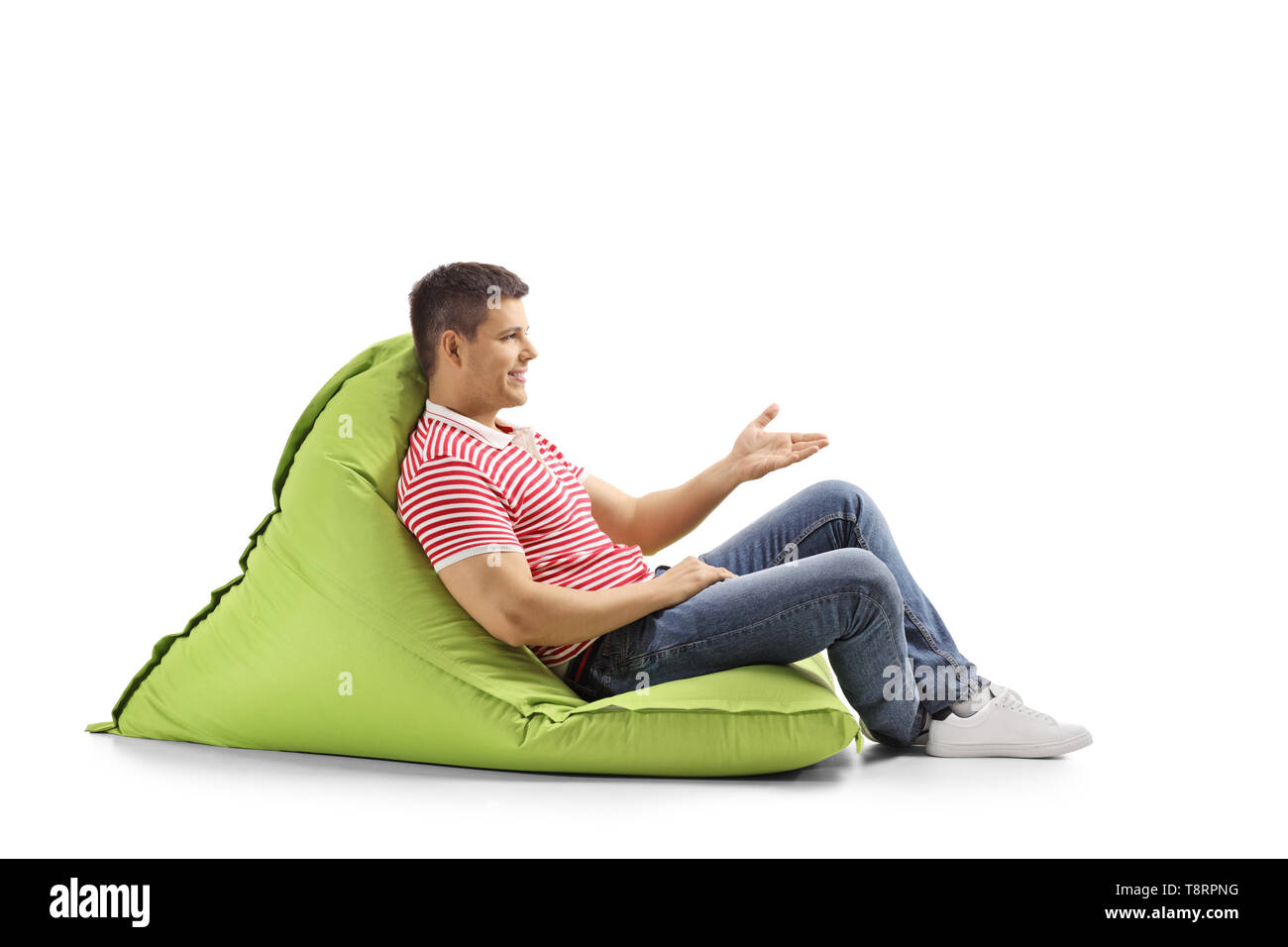 Lunghezza piena ripresa di profilo di un giovane uomo seduto su un verde bean bag e gesticolando con la mano isolati su sfondo bianco Foto Stock