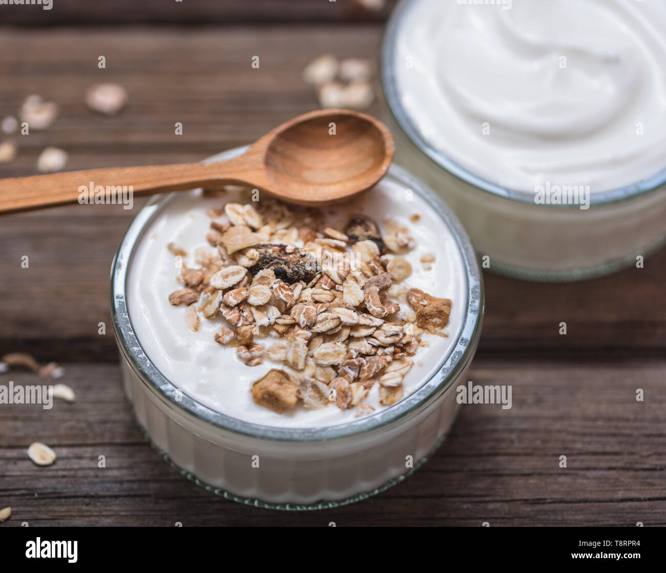 Yogurt bianco in recipiente di vetro su una vecchia scrivania in legno con il cucchiaio di legno sul lato superiore. Foto Stock