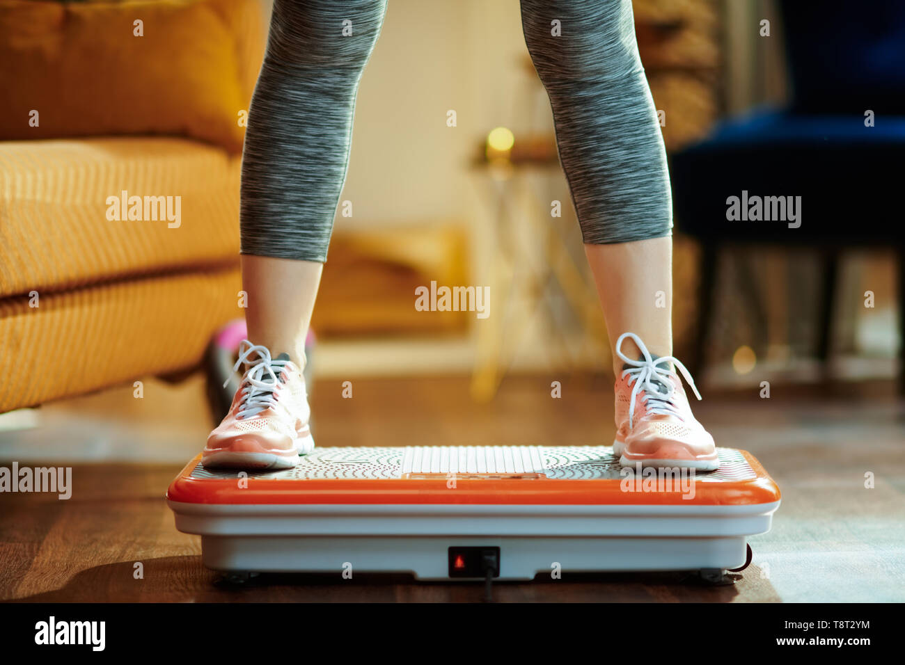 Primo piano sul giovane donna in abiti di fitness in casa moderna formazione utilizzando la vibrazione della piastra di alimentazione. Foto Stock