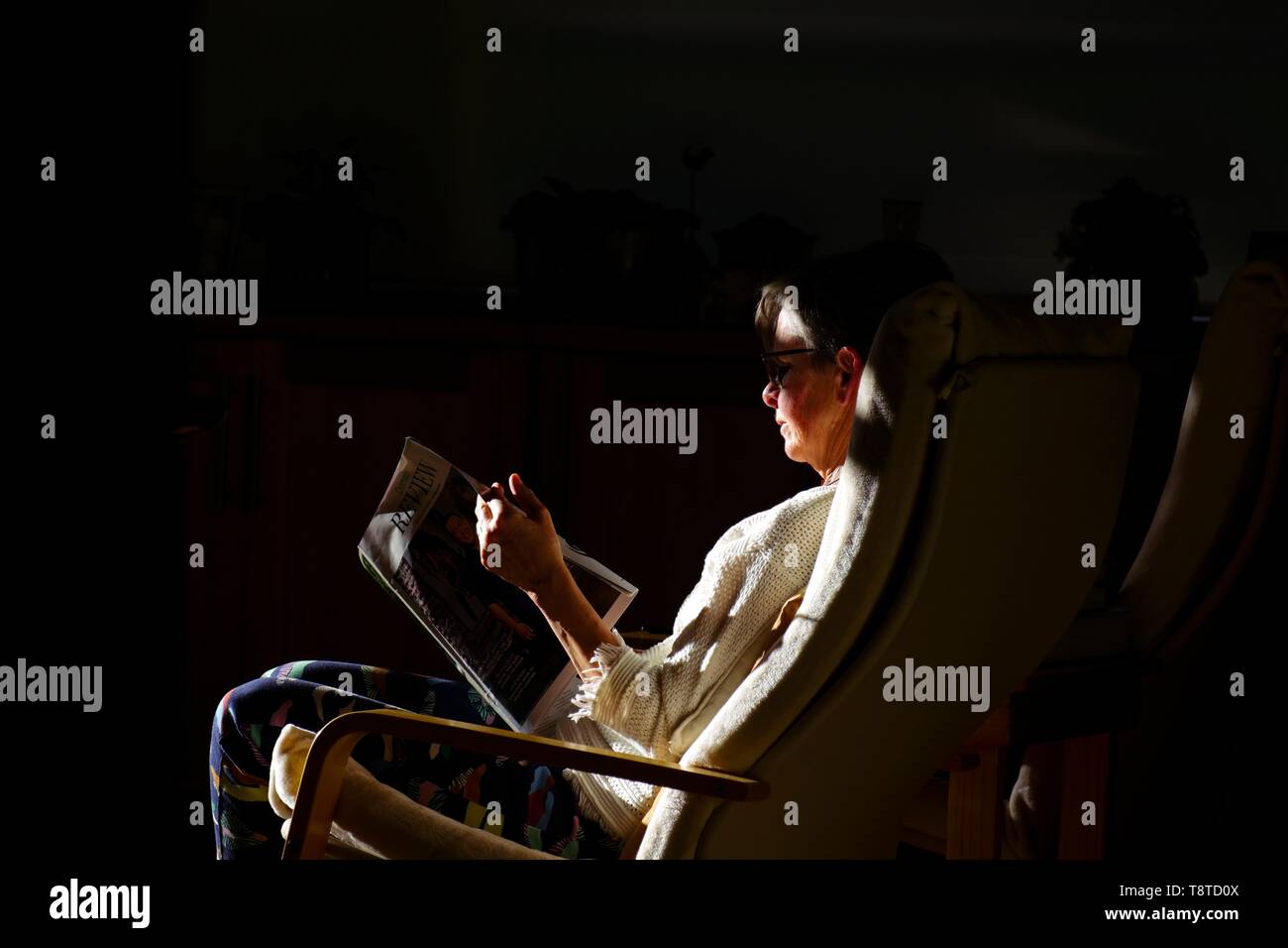 In cerca di illuminazione? Signora leggendo una rivista illuminata dal sole del tardo pomeriggio contro uno sfondo scuro. Foto Stock