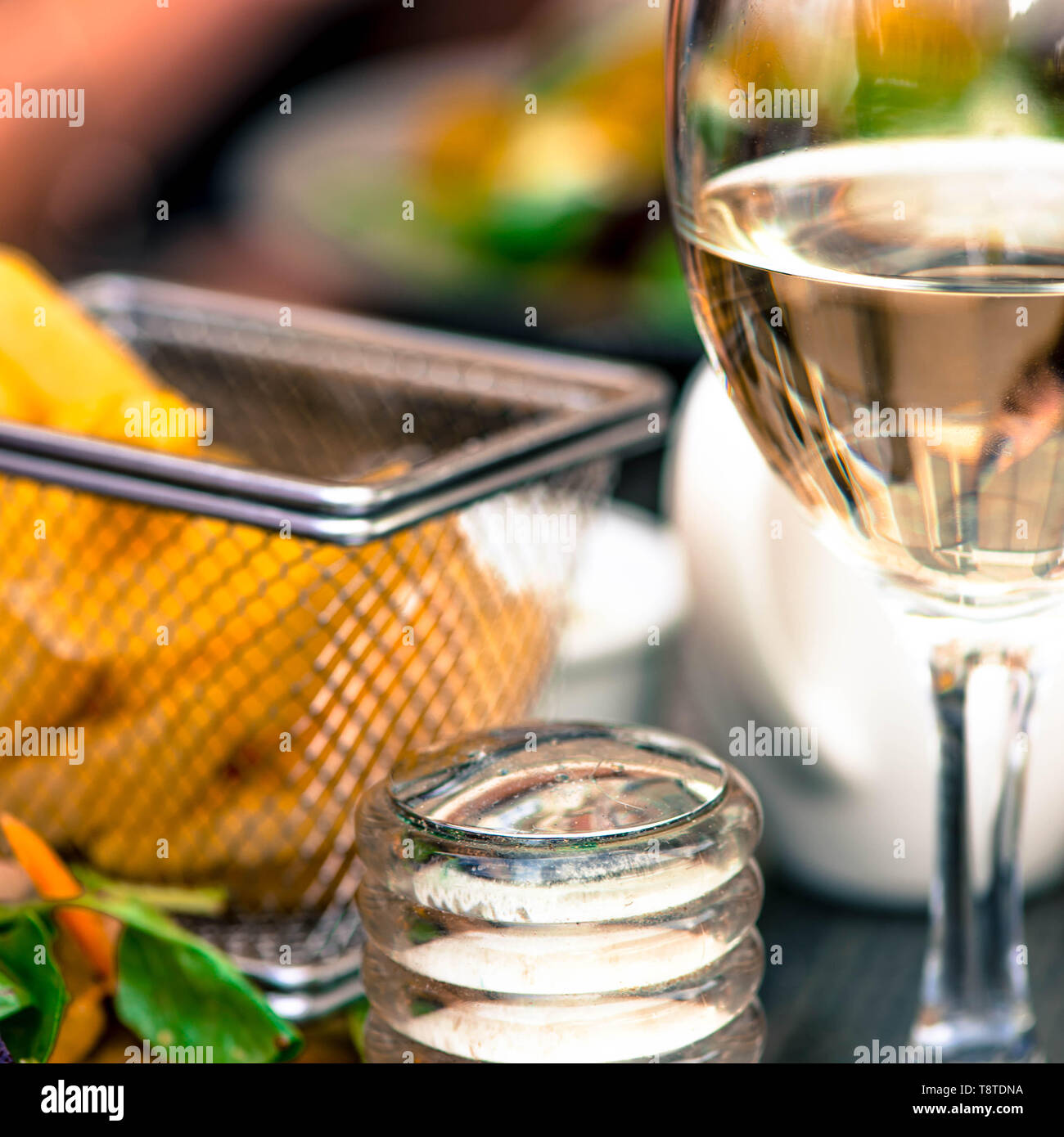 Bicchiere di vino bianco con un paniere di chip su una tabella di impostazione superiore Foto Stock