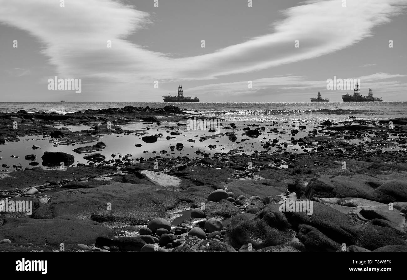 Il paesaggio della costa con la bassa marea, impianti di trivellazione del petrolio e il cielo nuvoloso, bianco e nero, baia di Las Palmas di Gran Canaria Foto Stock