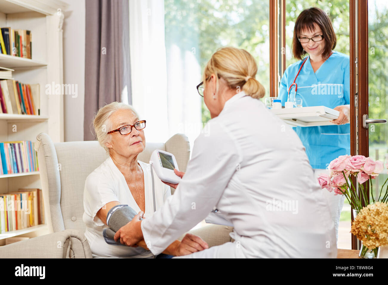 Medico donna misura la pressione del sangue come una misura precauzionale con un anziano nella sua Senior Citizen's home Foto Stock