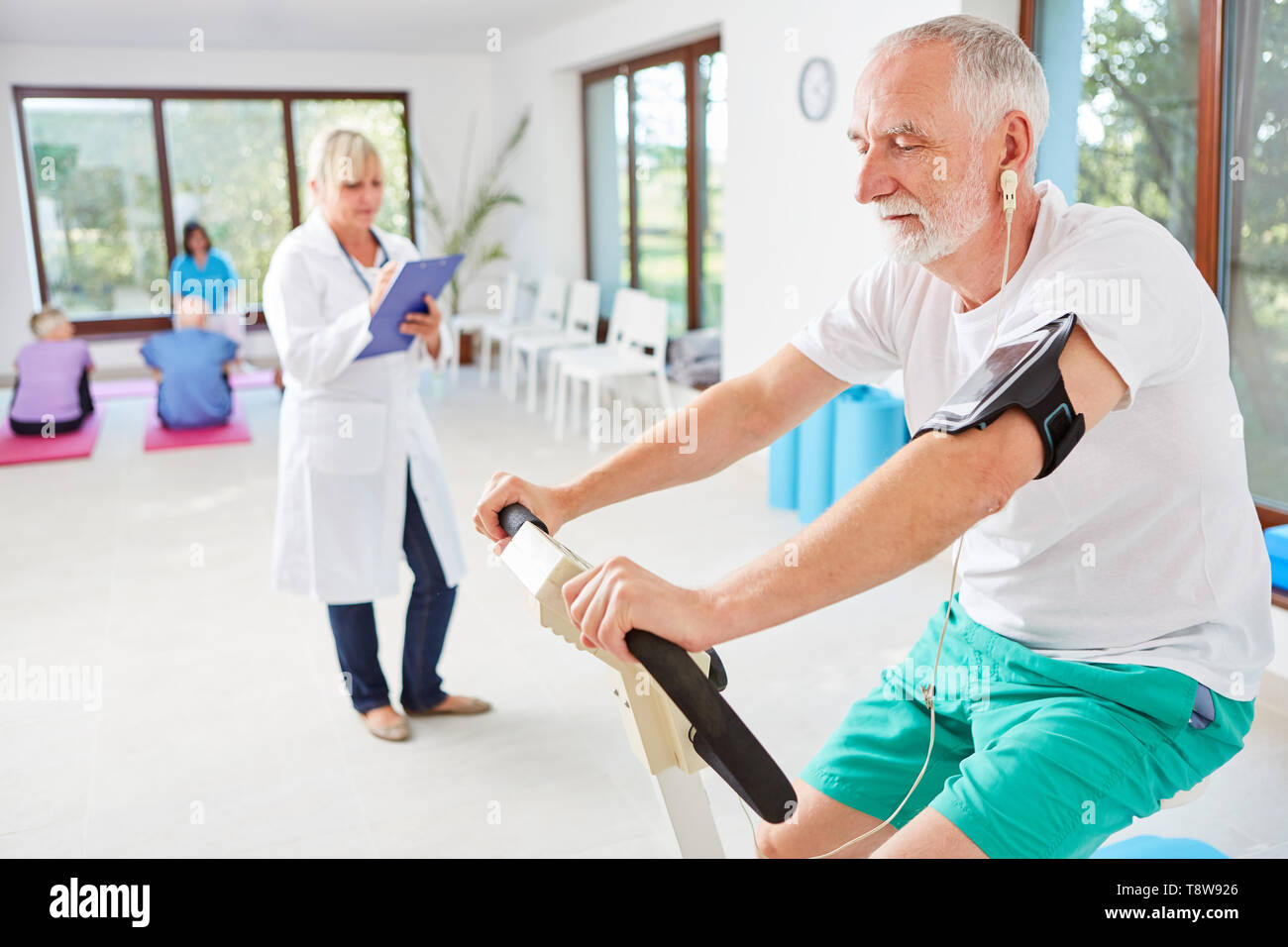 Uomo Senior in palestra Ergometro durante la formazione supervisionato da un medico di sesso femminile Foto Stock