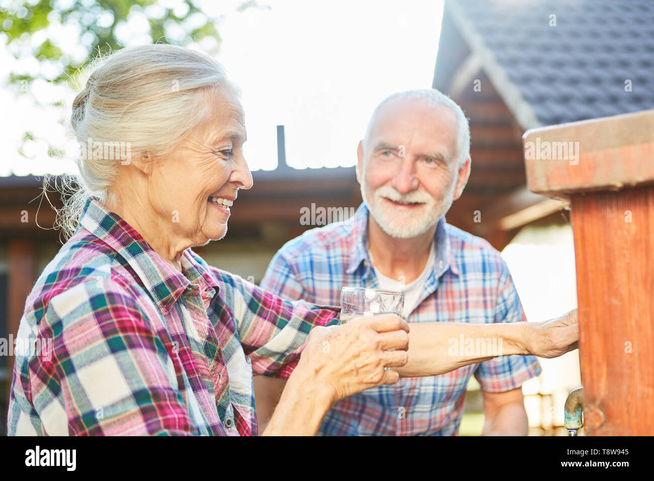 Senior Citizen beve un bicchiere di acqua ad un acqua toccando il punto in una fattoria Foto Stock