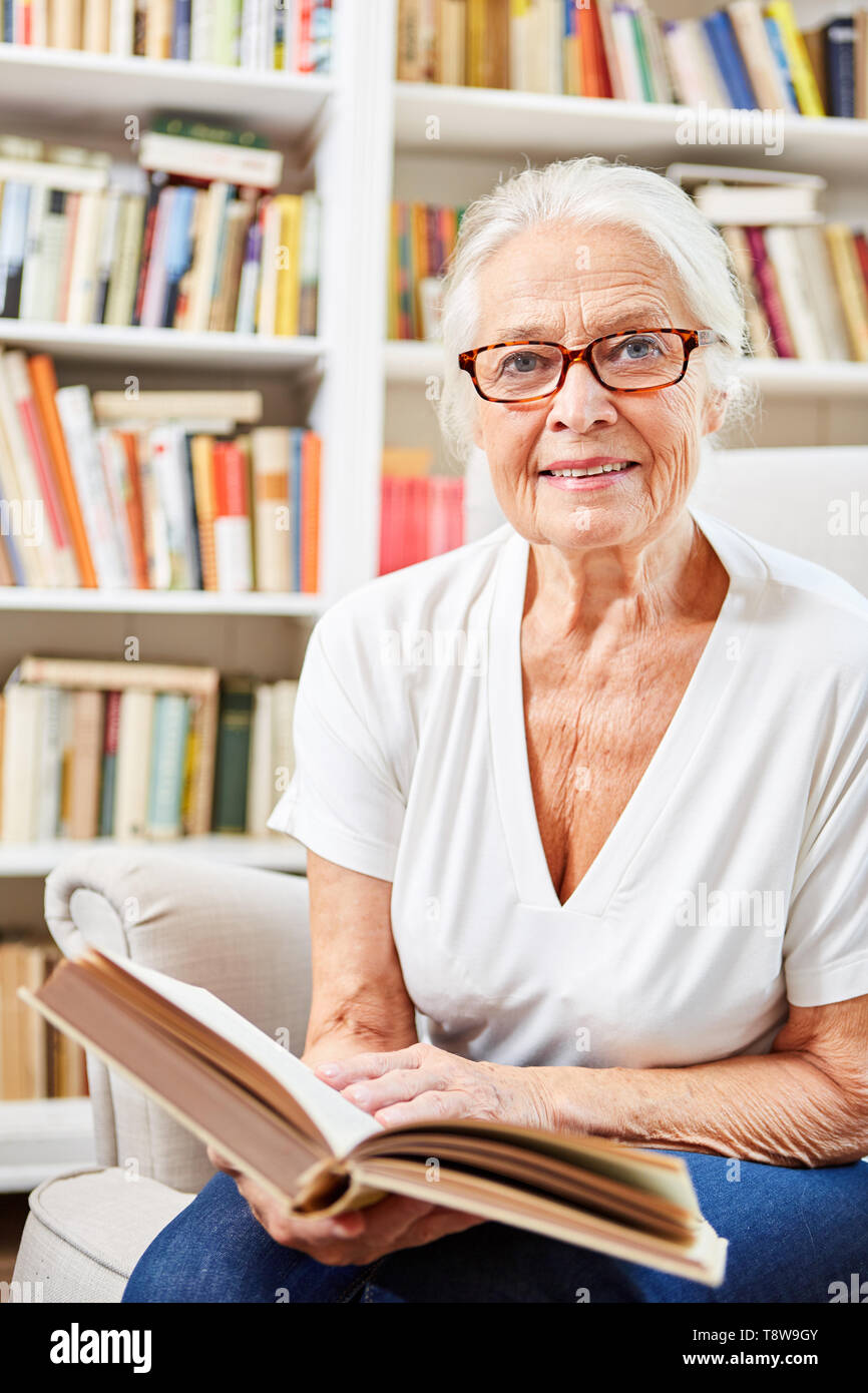 Sorridente donna senior è seduto con un libro nella libreria o nella libreria Foto Stock