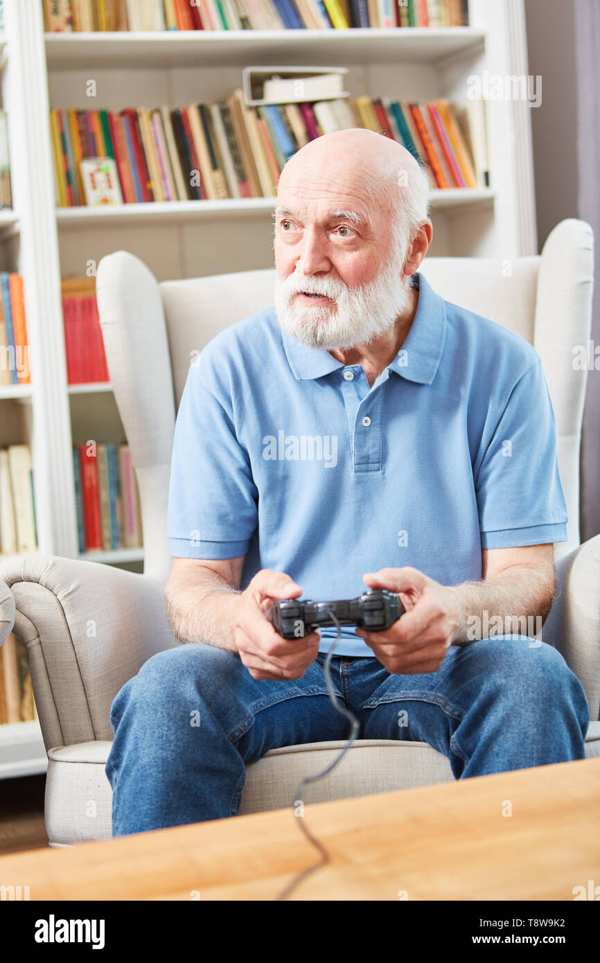 Senior uomo riproduce il video gioco con la console in salotto come occupazione Foto Stock
