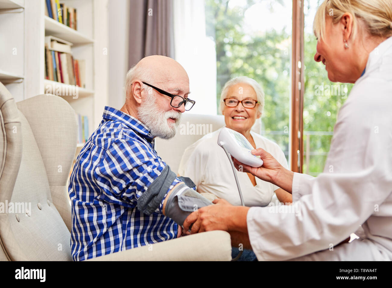 Medico donna controlla la pressione del sangue di un anziano nella sua senior citizen appartamento Foto Stock