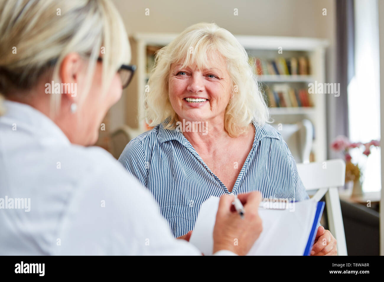 Medico con appunti e senior citizen come un paziente nel campo dell'assistenza infermieristica casa o visitare il sito web Foto Stock