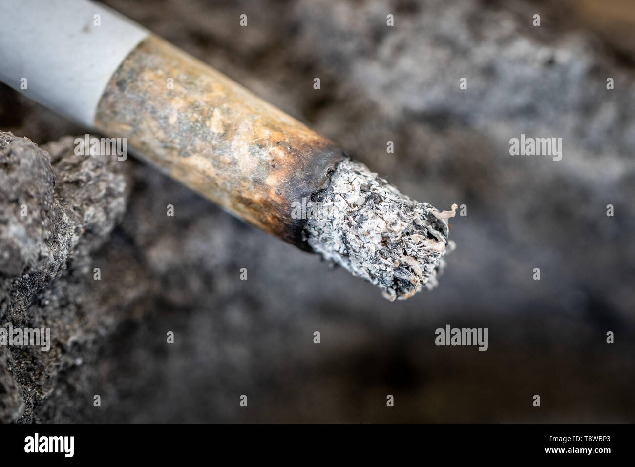 Una sigaretta senza fiamma con la cenere sul bordo di un posacenere fatta di lava solidificata. Close up. Foto Stock