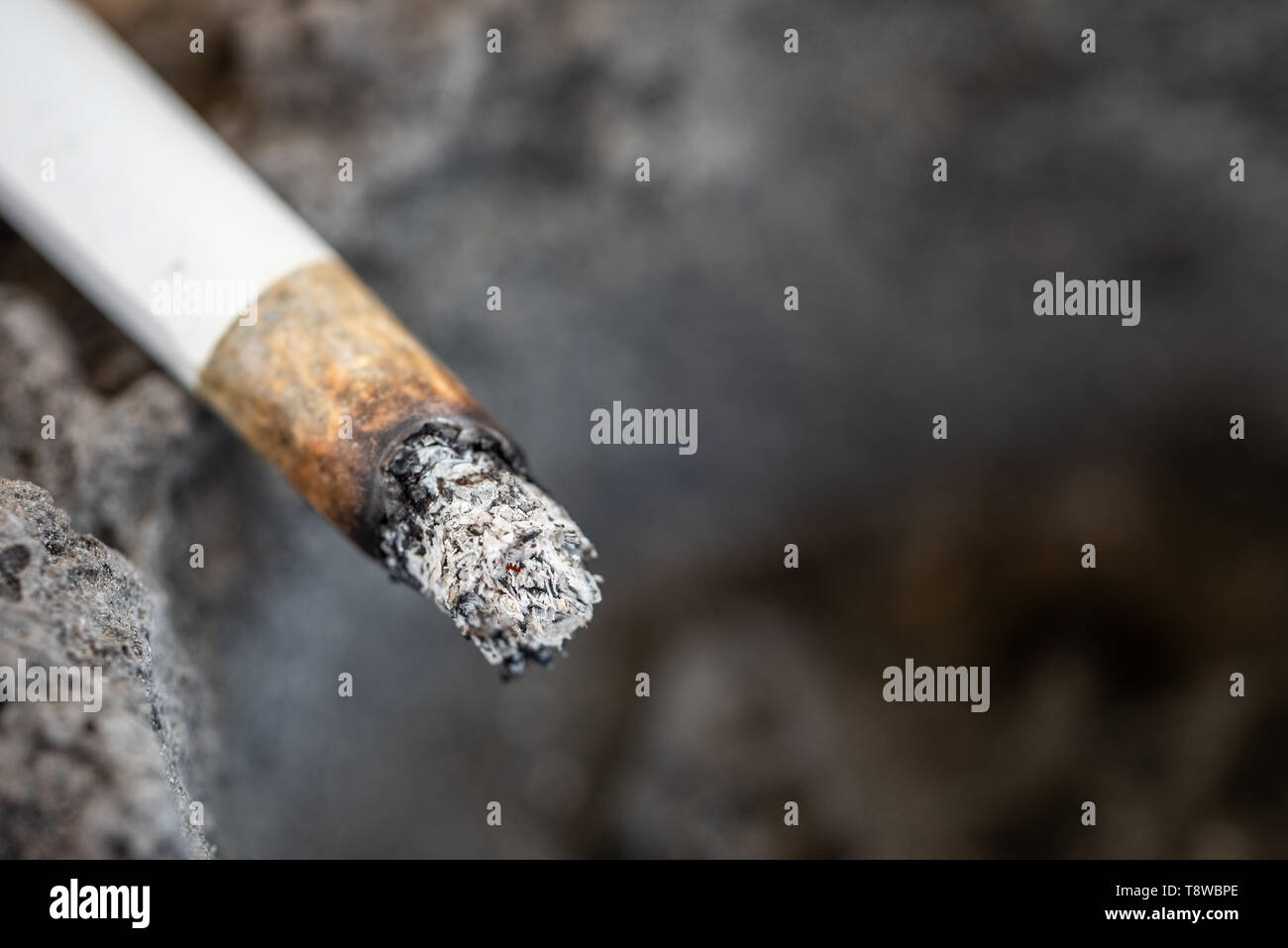 Una sigaretta senza fiamma con la cenere sul bordo di un posacenere fatta di lava solidificata. Close up. Copia dello spazio. Foto Stock