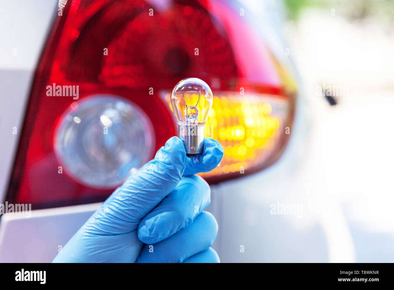 Una mano che tiene una lampadina per auto, lampada di coda in background Foto Stock