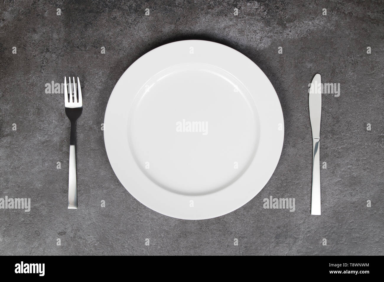 Bianco piastra vuota con coltello e forchetta su sfondo grigio Foto Stock