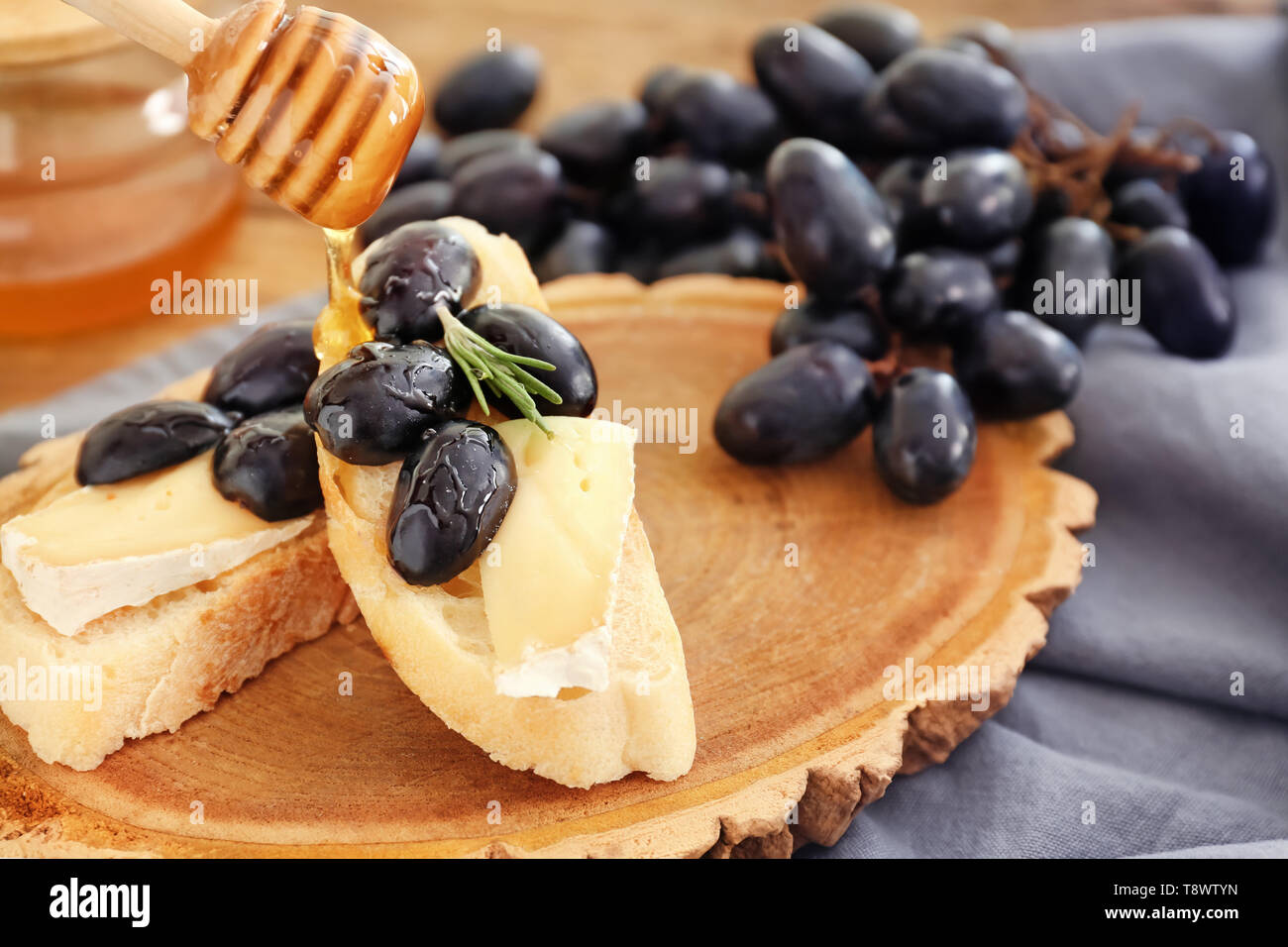 Il versamento del miele sul panino con il formaggio e i mosti di uve Foto Stock