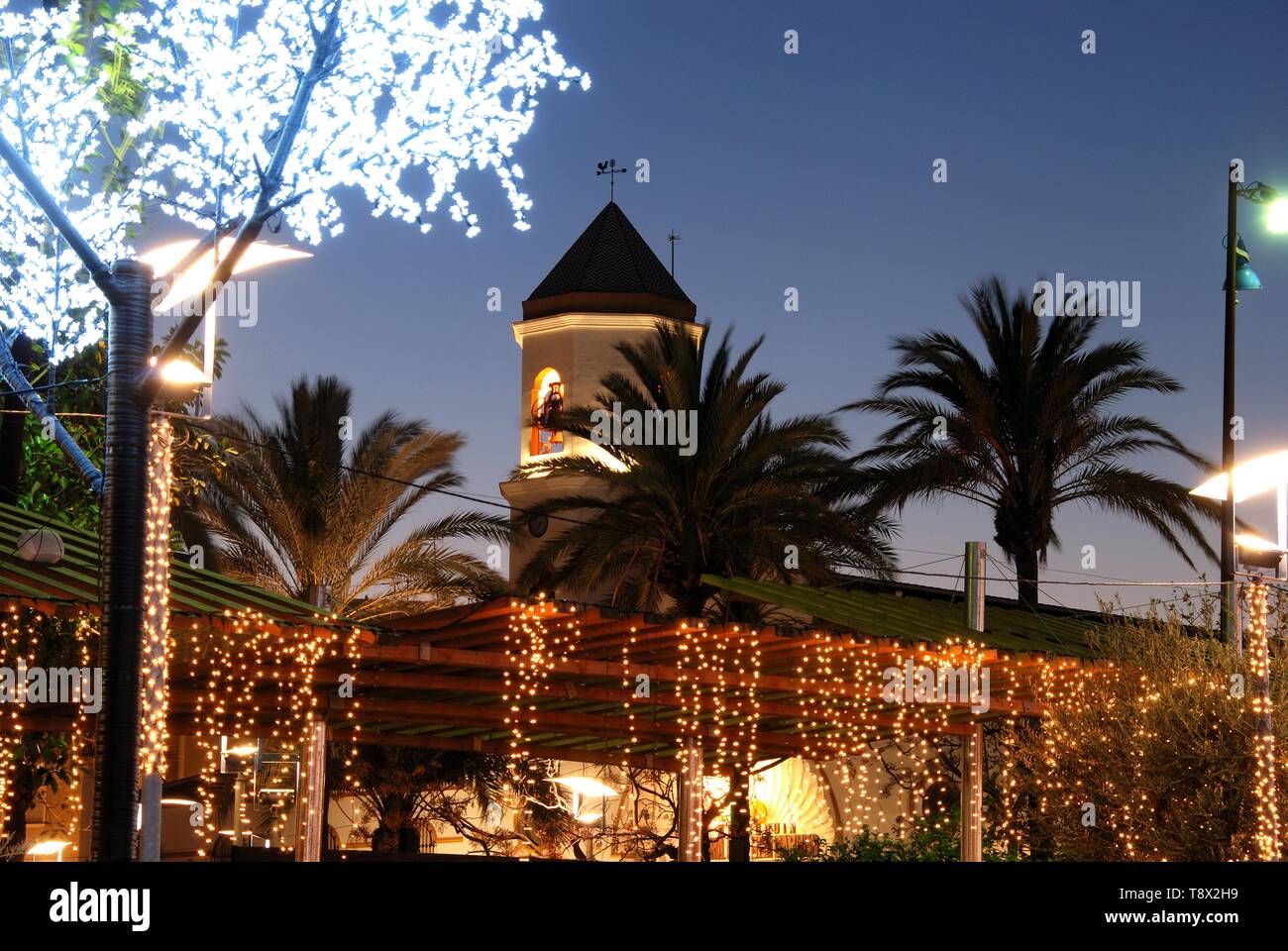 Le decorazioni di Natale in una piazza con la Chiesa di Carmen torre campanaria (Parroquia Nuestra Señora del Carmen) verso la parte posteriore, Fuengirola, Spagna. Foto Stock
