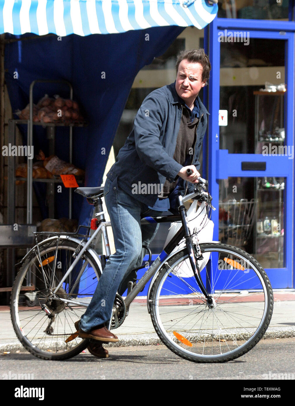 David Cameron è chiaramente un uomo della sua parola come egli usa la sua moto per fare la famiglia a fare la spesa presso i suoi negozi locali. Chiaramente non è per il sig. Cameron è il 'celebrità stile' supermercato consegne di stile come il 'moderne man' carichi la sua bicicletta in un vero sinistra/destra bilanciamento atto come egli ruotata a destra di fronte un juuggernaut! La prossima volta forse un insieme di ciclismo ingranaggio di sicurezza potrebbe essere appropriato. Foto di Tony Henshaw Foto Stock