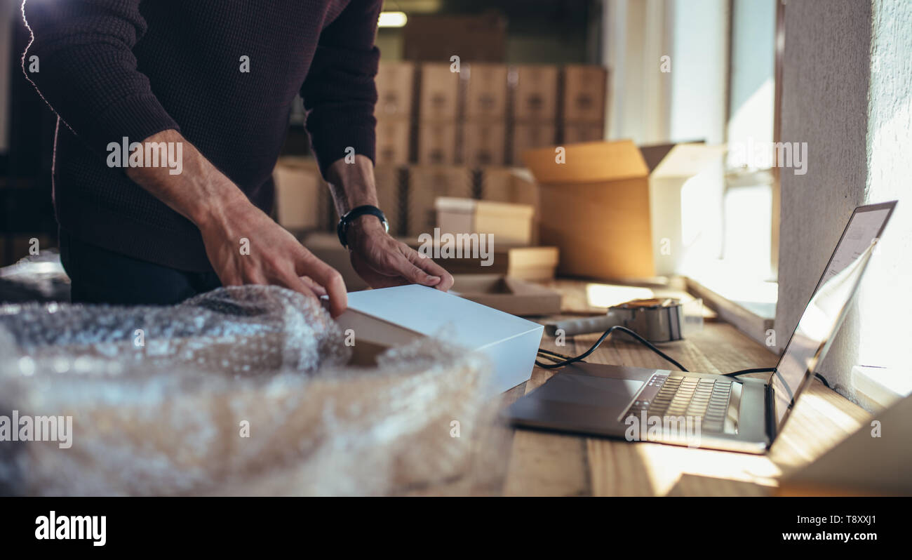 Titolare di una piccola azienda di imballaggio il cardbox al posto di lavoro. Ritagliato shot dell uomo la preparazione di un pacco per la consegna alla vendita online business office. Foto Stock