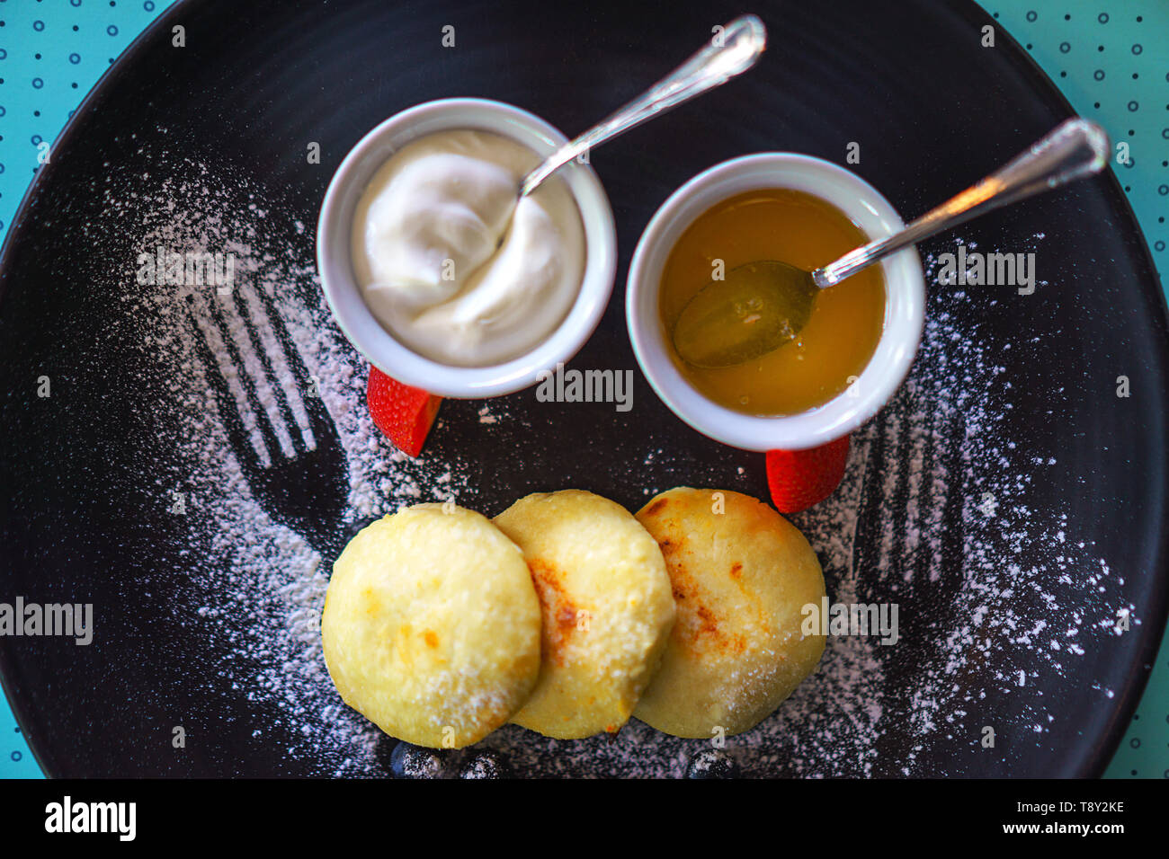 Una sana colazione cottage cheesecake sirniki russo con miele e panna acida per la colazione su sfondo blu. Foto Stock