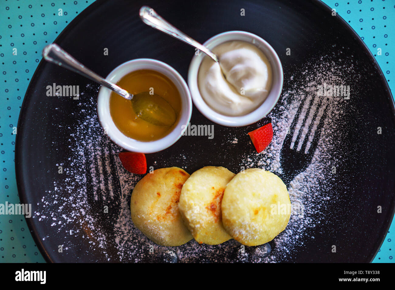 Una sana colazione cottage cheesecake sirniki russo con miele e panna acida per la colazione su sfondo blu. Foto Stock