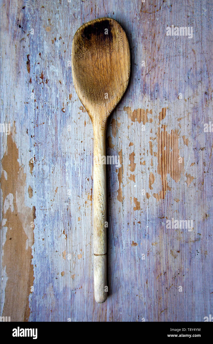 Un cucchiaio di legno ben usato su uno sfondo di legno dipinto. Foto Stock