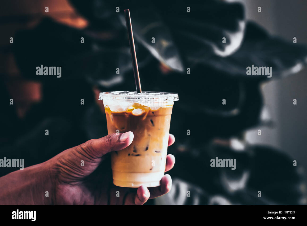 Tenere in mano il caffè di ghiaccio in un bicchiere alto con panna versato sopra e i chicchi di caffè in una natura verde di lasciare il tono scuro. Cold drink estivo sullo sfondo Foto Stock