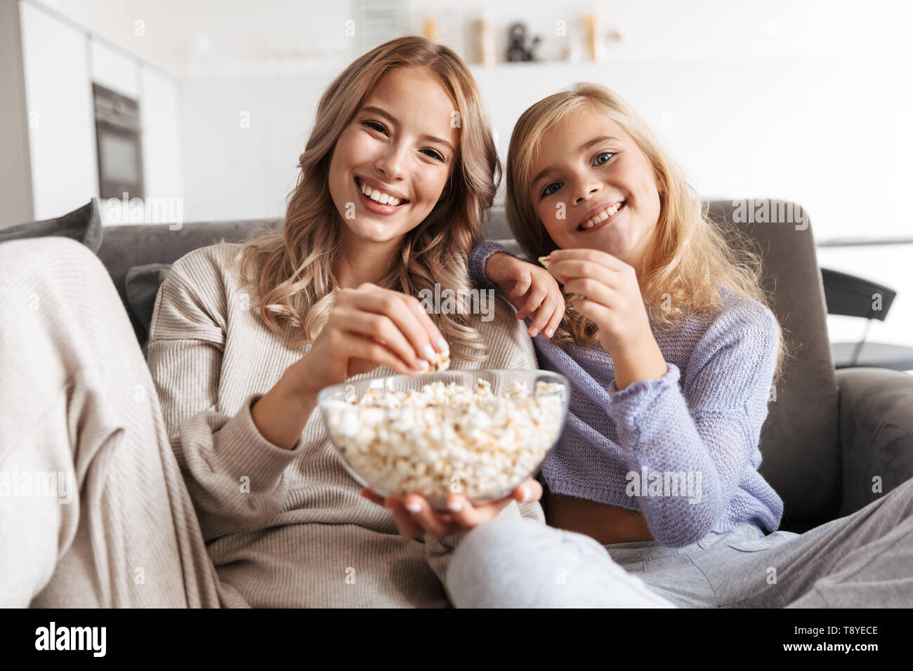 Immagine di un felice giovane donna con la sua sorellina in interni a casa per guardare la tv mangiare popcorn. Foto Stock