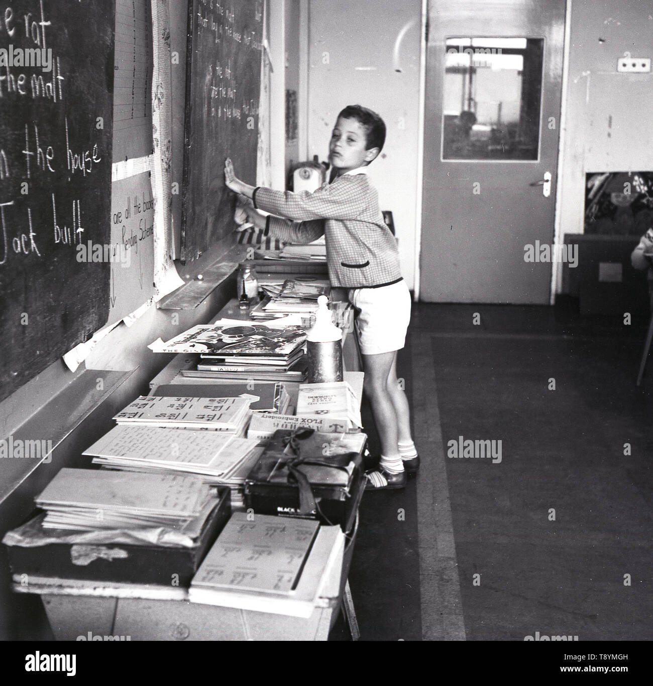 Anni sessanta, storico, giovane scolaro tergi chalk iscritto off blackboard lato in un aula scolastica, Inghilterra, Regno Unito. Foto Stock