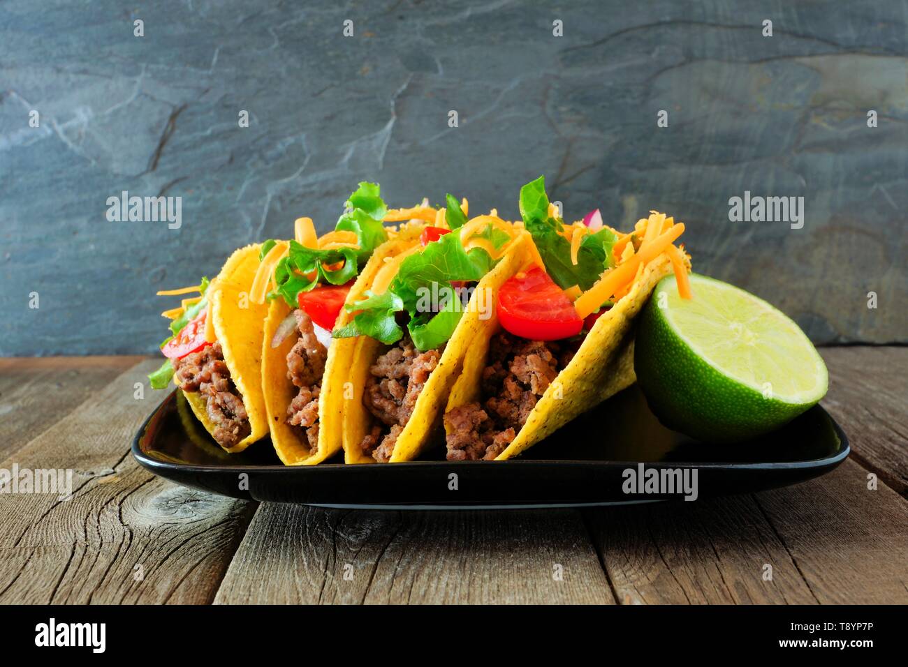 Disco sgusciate tacos con carne di manzo macinata, lattuga, pomodoro e formaggio. Gruppo sulla piastra con uno sfondo scuro. Foto Stock