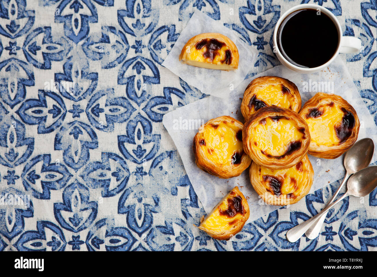 Uovo tart, tradizionale dolce portoghese, Pastel de nata su una carta pergamena. Sfondo blu. Vista dall'alto. Copia dello spazio. Foto Stock