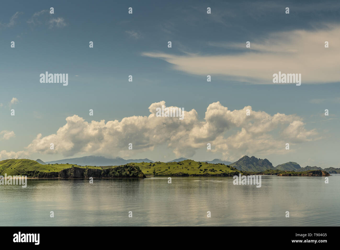 Isola di Rinca, Indonesia - 24 Febbraio 2019: Piana isolette off Westside costa in mare Savu sotto cloudscape con macchie bianche. Verde delle colline in distanza a Foto Stock