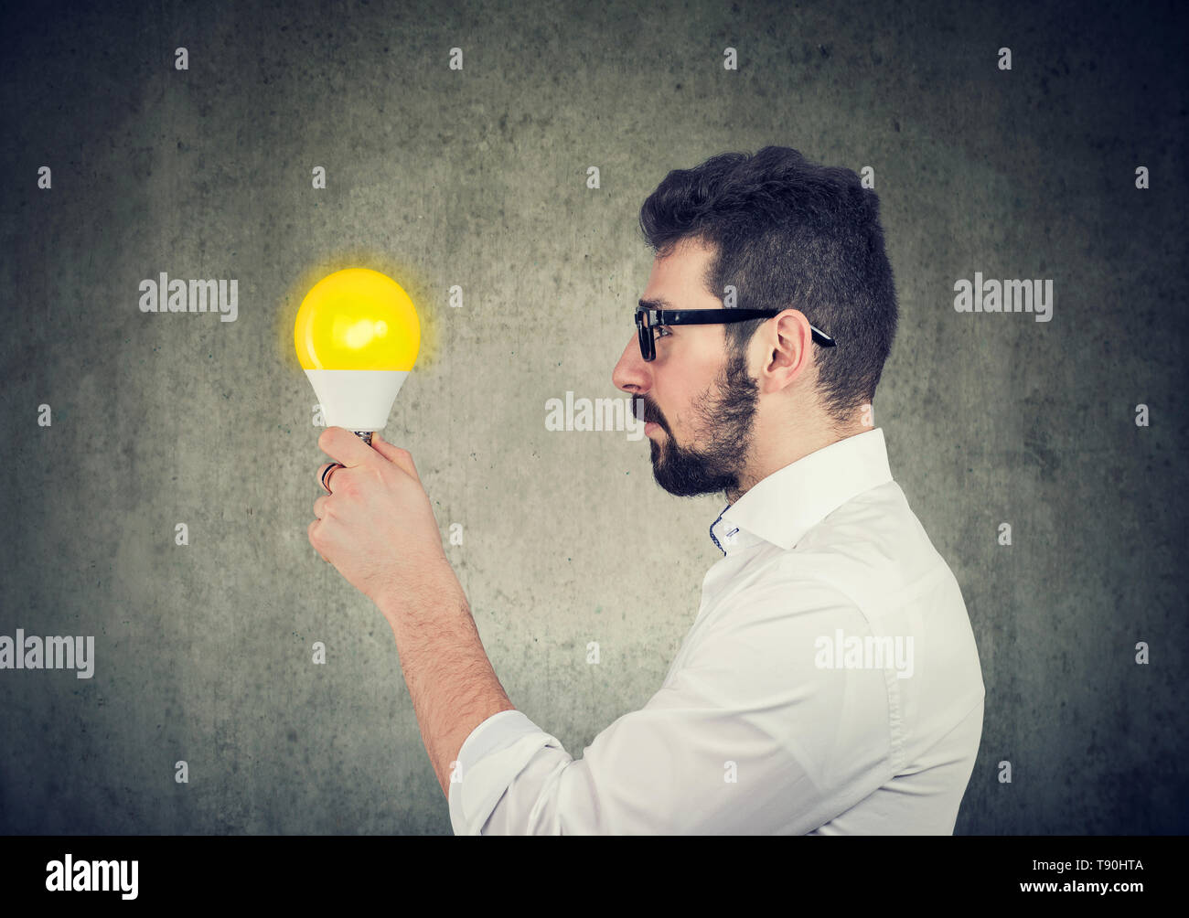 Giovane uomo d affari con espressione pensosa guardando alla luce brillante lampadina Foto Stock