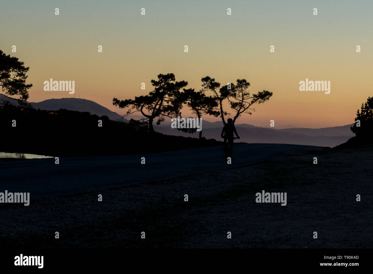Silhouette di un uomo in sella ad una bicicletta su per la montagna al tramonto Foto Stock