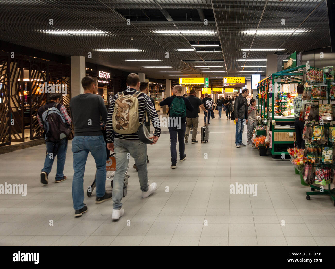 I passeggeri del trasporto aereo a passeggio tra negozi e ristoranti attraverso uno dei principali councourses dell'aeroporto Schiphol di Amsterdam Foto Stock