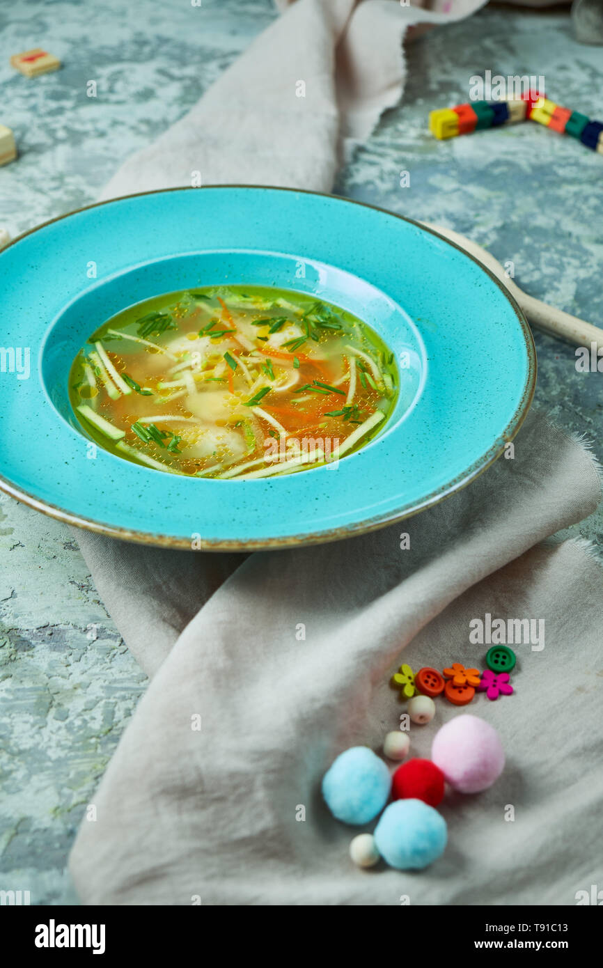 Zuppa di pollo con verdi in una piastra di blu. Su un grigio sfondo a trama. Menu per bambini. Bella che serve dei piatti. Foto Stock
