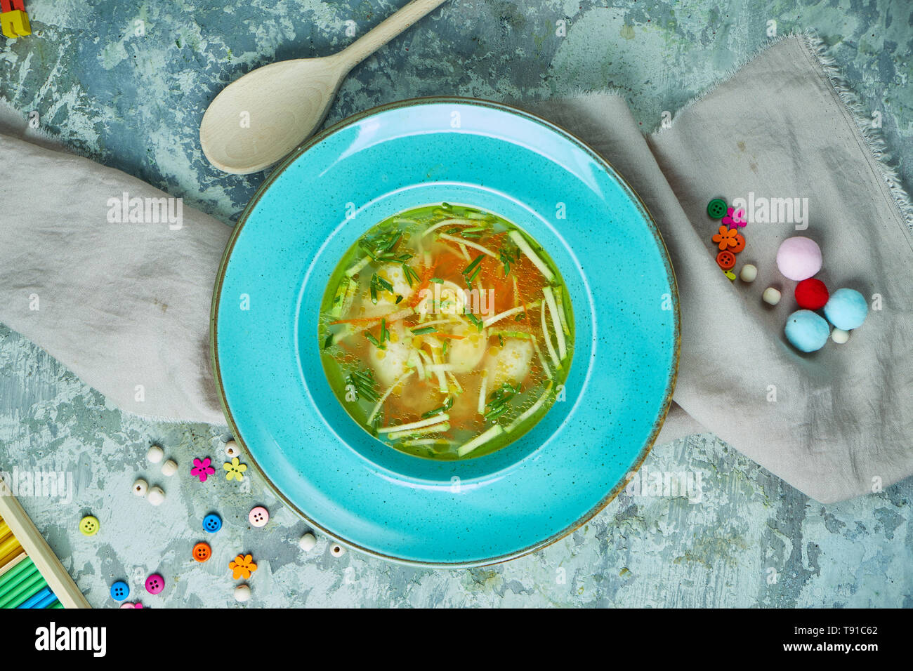 Zuppa di pollo con verdi in una piastra di blu. Su un grigio sfondo a trama. Menu per bambini. Bella che serve dei piatti. Foto Stock